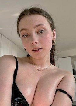 Petite brunette in shiny black strapless top takes selfie in kitchen.