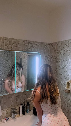 Woman with long hair in a bathroom taking a selfie in a mirror.