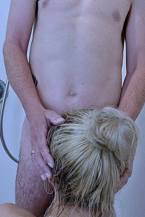 Bare-chested man with pubic hair and side tattoo grips blonde woman's hair bun from behind in shower.
