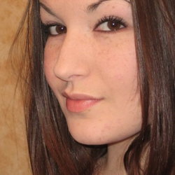 Close-up of a woman with long dark brown hair, freckles, and soft makeup, looking slightly to the side against a