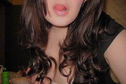 Close-up of a woman with long dark wavy hair, wearing a black top, lips slightly parted, in an indoor setting.