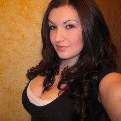 Brunette woman with long dark hair takes a selfie in a black top.