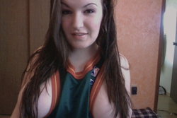 Brunette woman in a sports jersey posing in a dimly lit room.