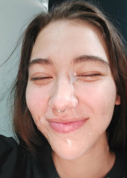 Close-up selfie of a woman with brown hair, nose ring, and white substance on her face, smiling with eyes closed