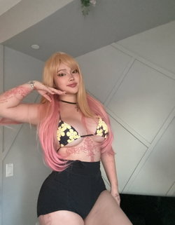 Blonde woman with pink hair extensions poses in a floral bralette and black skirt.